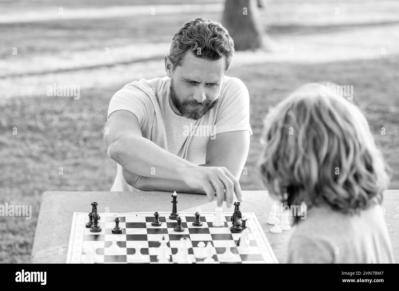 Glückliche Familie von Vater und Sohn Kind spielen Schach auf dem Tisch im Park im Freien, analytisches Denken Stockfoto