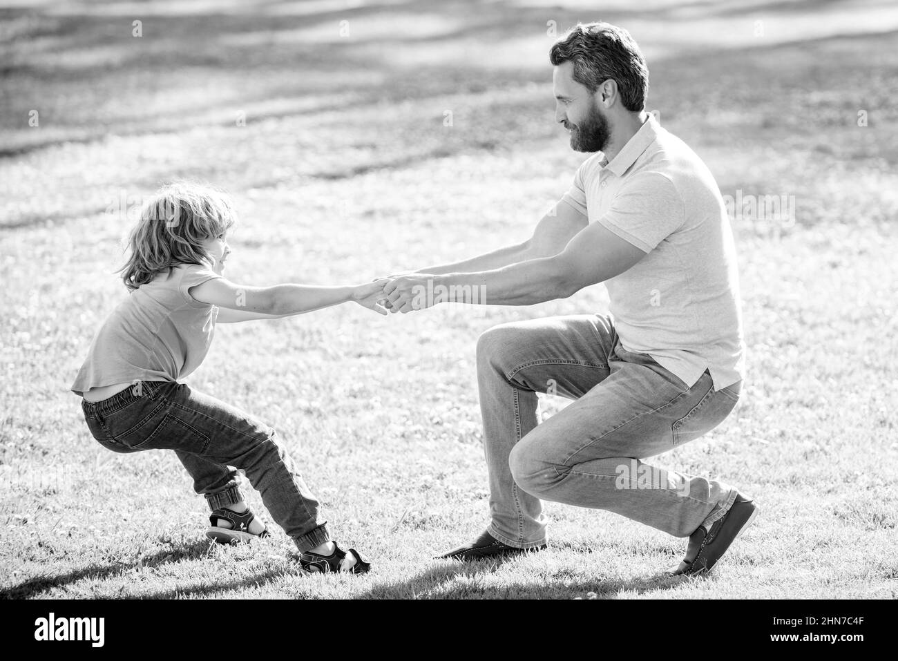 Zeit zum Spielen. Glücklicher Sohn zieht dem Vater die Hände. Junge Kind und Mann spielen Sommer im Freien. Spaß für die ganze Familie Stockfoto