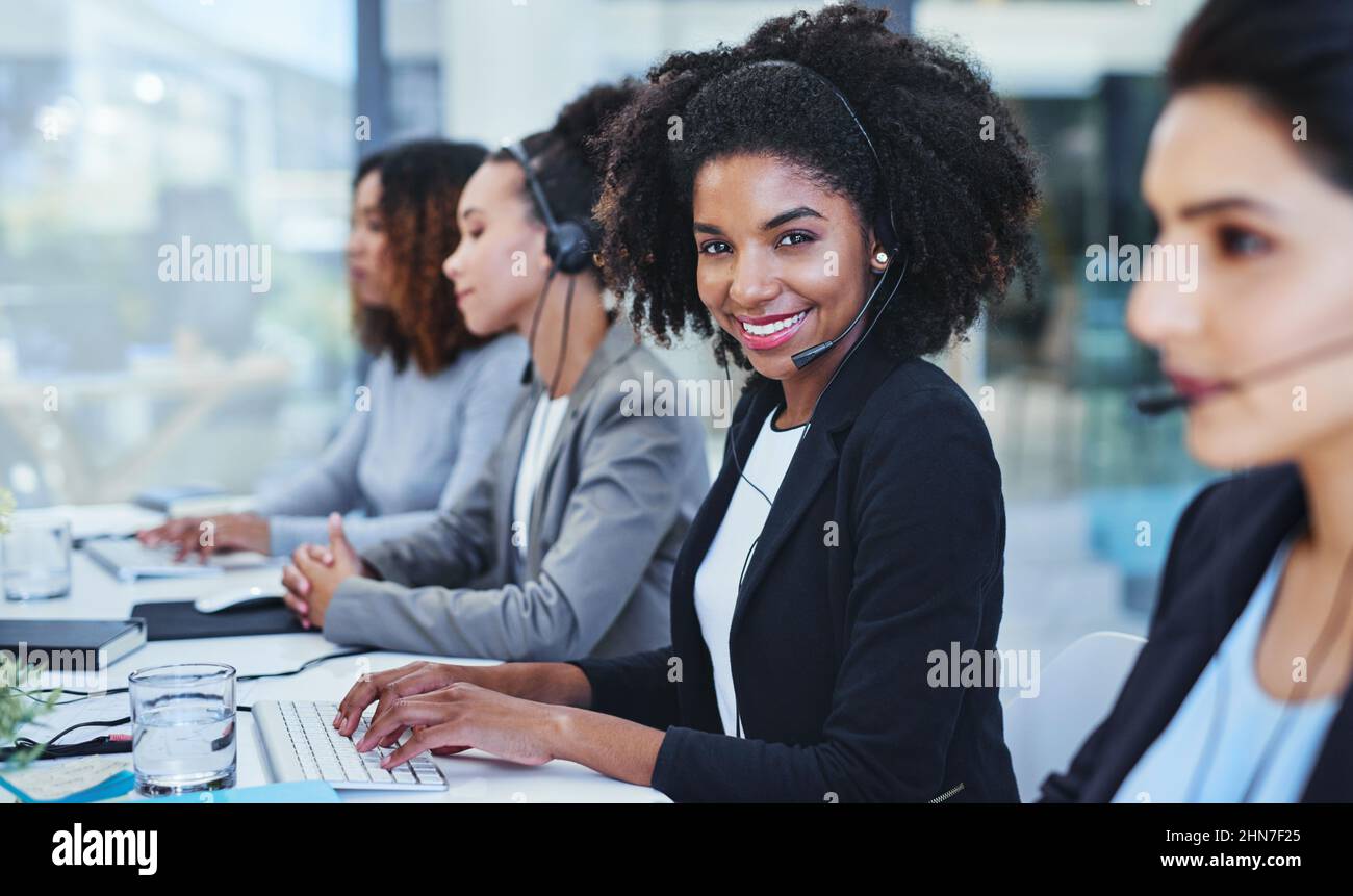 Hier und gerne helfen. Porträt einer jungen Frau, die zusammen mit ihren Kollegen in einem Callcenter arbeitet. Stockfoto