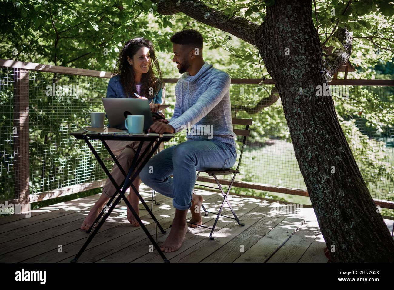 Glückliches Paar mit einem Laptop, der sich im Freien in einem Baumhaus, einem Wochenendausflug und einem Remote-Office-Konzept ausruhen kann. Stockfoto