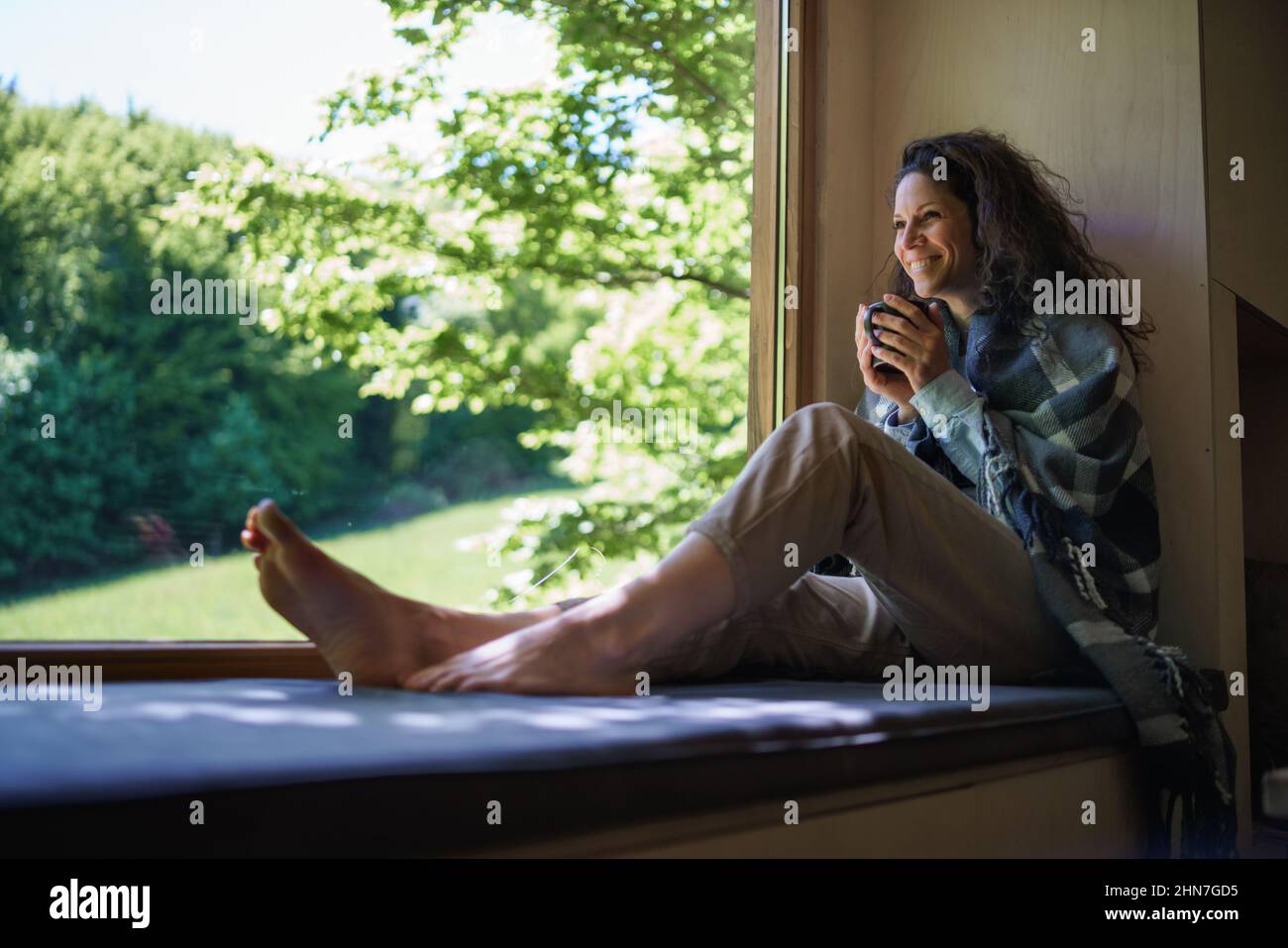 Glückliche Frau mit Kaffee, die drinnen in einem Baumhaus sitzt, Wochenendausflug und digitales Entgiftungskonzept. Stockfoto