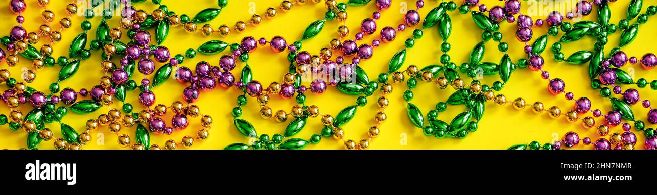 Mardi Gras Konzept. Bunte Perlen auf gelbem Hintergrund. Festliche Karnevalssymbole. Goldene grüne und violette Dekorationen für den Urlaub. Bannerformat, Stockfoto