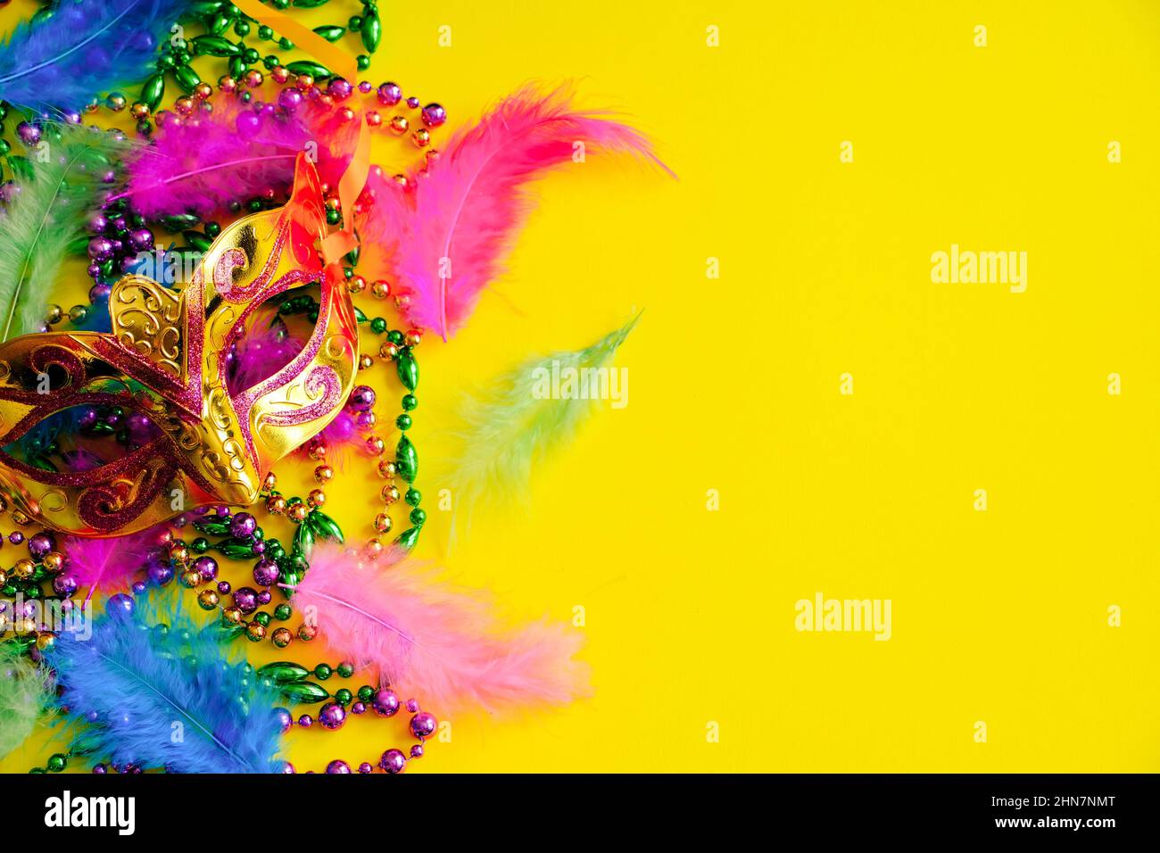 Karnevalsmaske mit Federn auf gelbem Hintergrund. Bunte Perlen in grün, Gold und lila. Symbol „Mardi Gras“ oder „Fat Tuesday“. Speicherplatz kopieren. Stockfoto