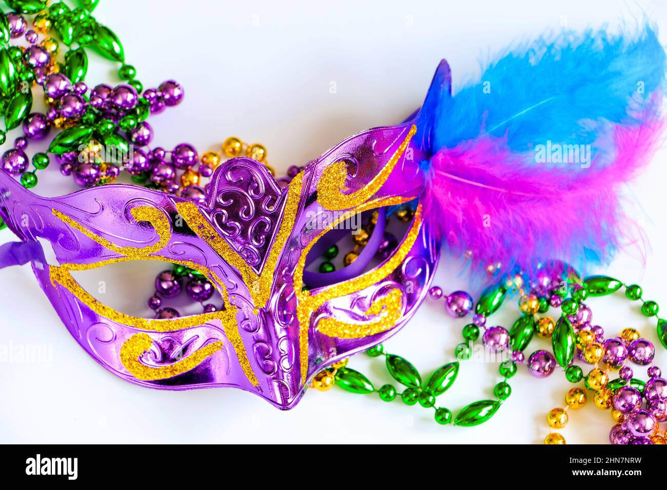 Lila Karnevalsmaske mit Federn und bunten Perlen aus nächster Nähe. Symbol „Mardi Gras“ oder „Fat Tuesday“. Festliche Dekorationen für traditionelle Feiertage. Stockfoto