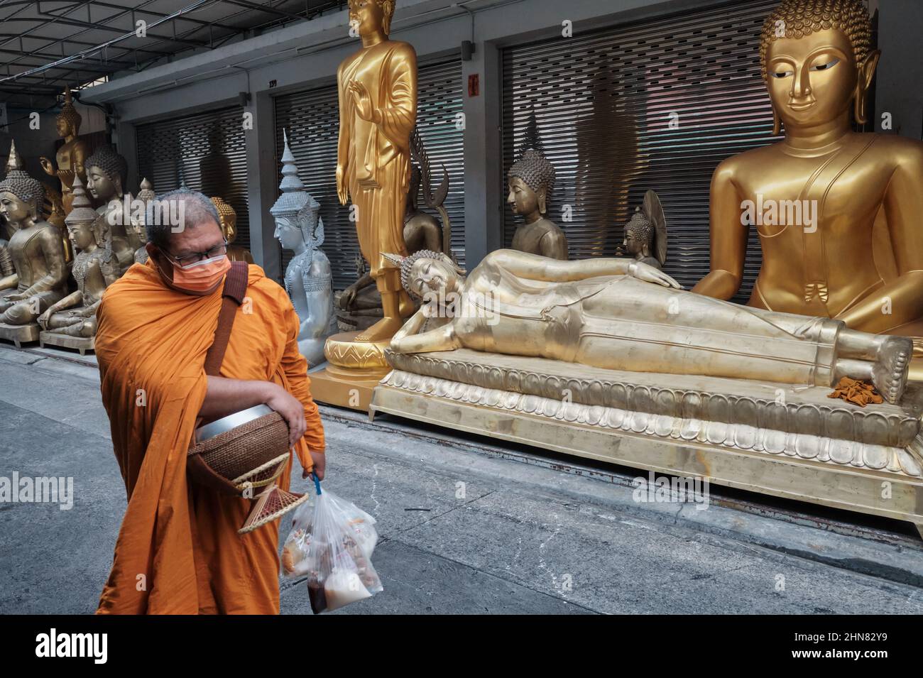 Ein thailändischer buddhistischer Mönch passiert einen schlafenden Buddha eine andere Buddha-Statue, die vor einem Geschäft für buddhistische Gegenstände aufgestellt ist; Bamrung Muang Rd., Bangkok, Thailand Stockfoto