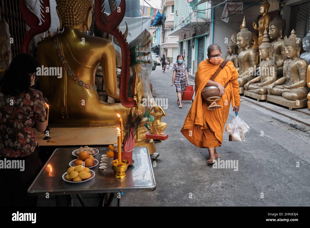 Ein thailändischer buddhistischer Mönch passiert schändliche Buddha-Statuen, die außerhalb des Shosp für buddhistische Objekte platziert sind; Bamrung Muang Rd., Bangkok, Thailand Stockfoto