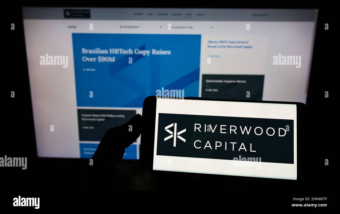 Person, die Smartphone mit dem Logo des US-Unternehmens Riverwood Capital Management L.P. auf dem Bildschirm vor der Website hält. Konzentrieren Sie sich auf die Telefonanzeige. Stockfoto