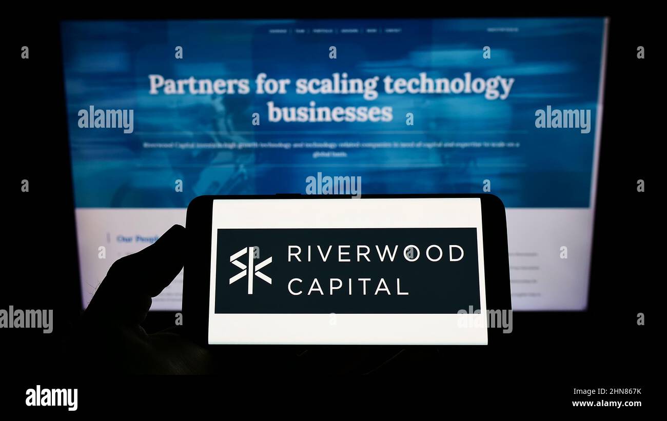 Person mit Mobiltelefon und Logo des amerikanischen Unternehmens Riverwood Capital Management LP auf dem Bildschirm vor der Webseite. Konzentrieren Sie sich auf die Telefonanzeige. Stockfoto