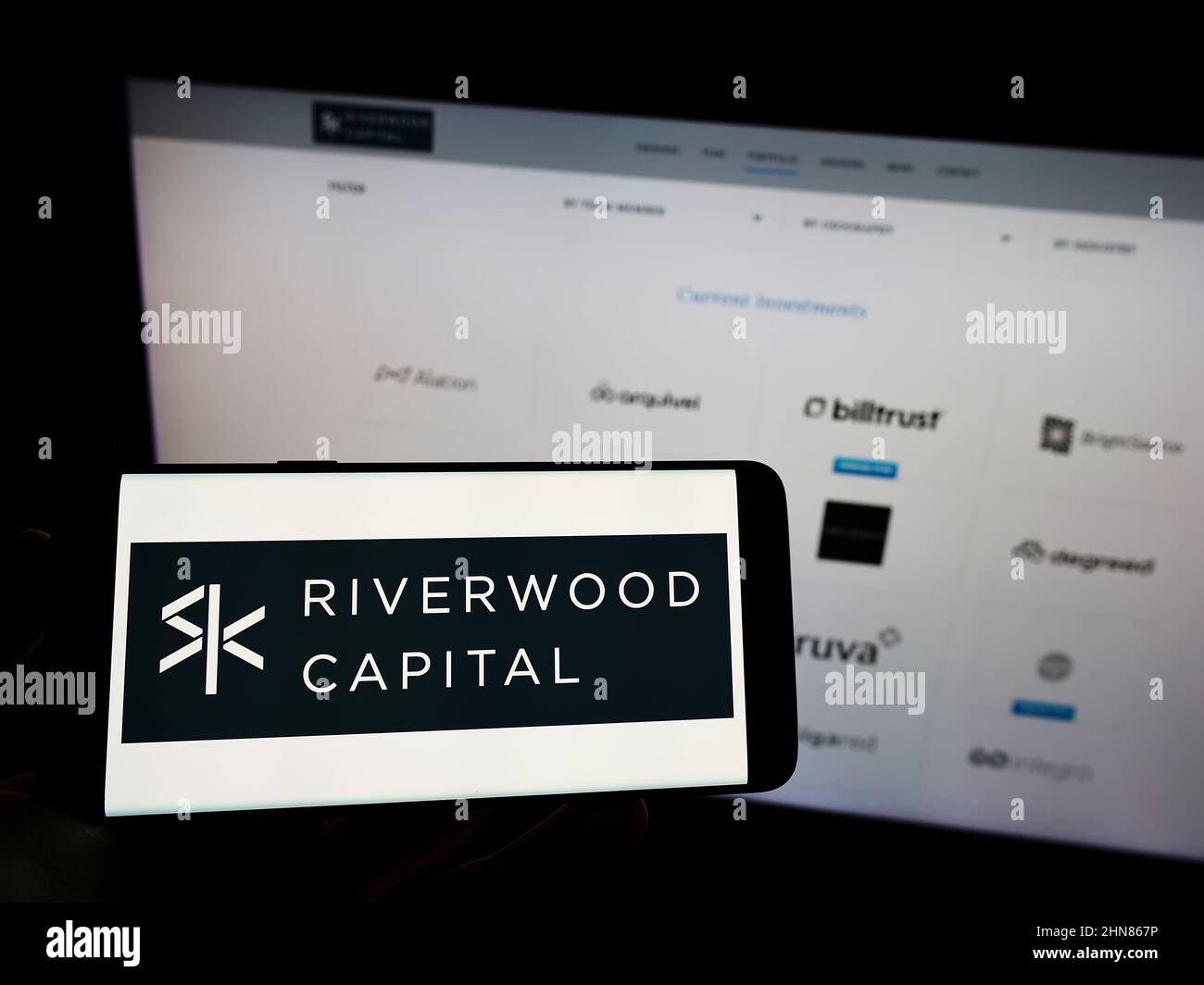 Person, die Mobiltelefon mit dem Logo des US-Unternehmens Riverwood Capital Management L.P. auf dem Bildschirm vor der Business-Webseite hält. Konzentrieren Sie sich auf die Telefonanzeige. Stockfoto