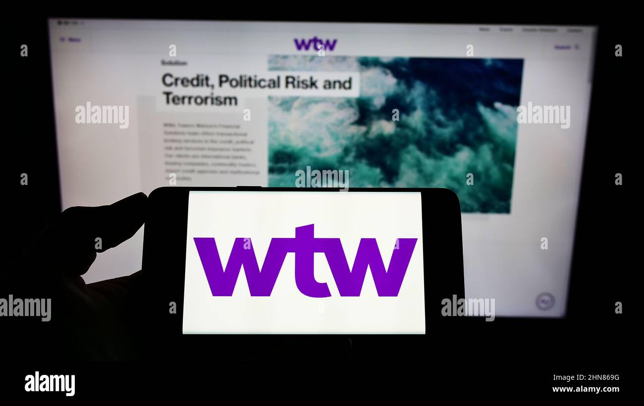 Person, die ein Mobiltelefon mit dem Logo des Finanzunternehmens Willis Towers Watson plc (WTW) auf dem Bildschirm vor der Webseite hält. Konzentrieren Sie sich auf die Telefonanzeige. Stockfoto