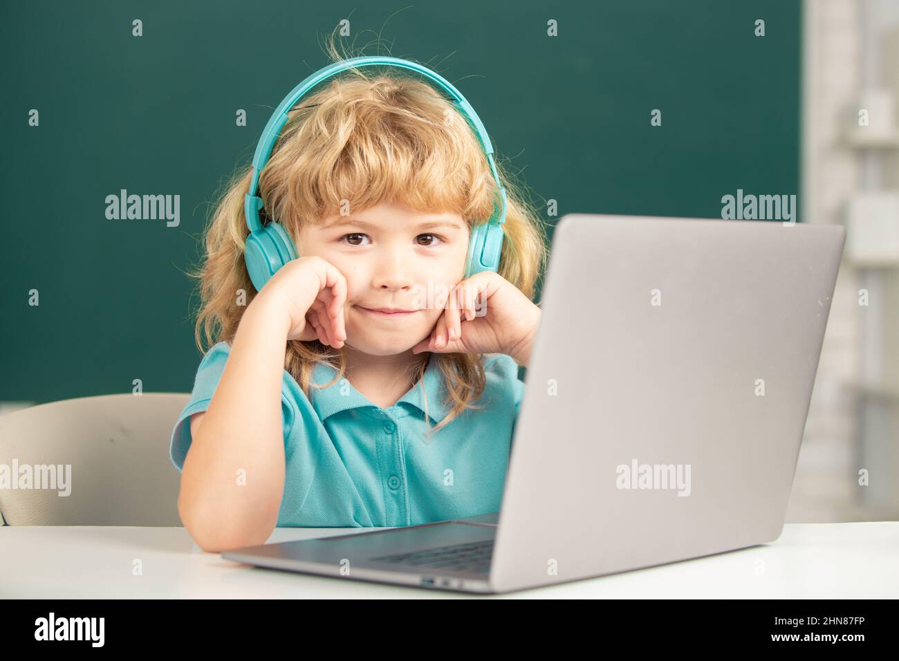 Cleverer Schuljunge, niedlicher Schüler trägt Kopfhörer, die auf dem Laptop schreiben, hören Sie Audiounterricht am Computer. Grundschule und Bildung. Stockfoto