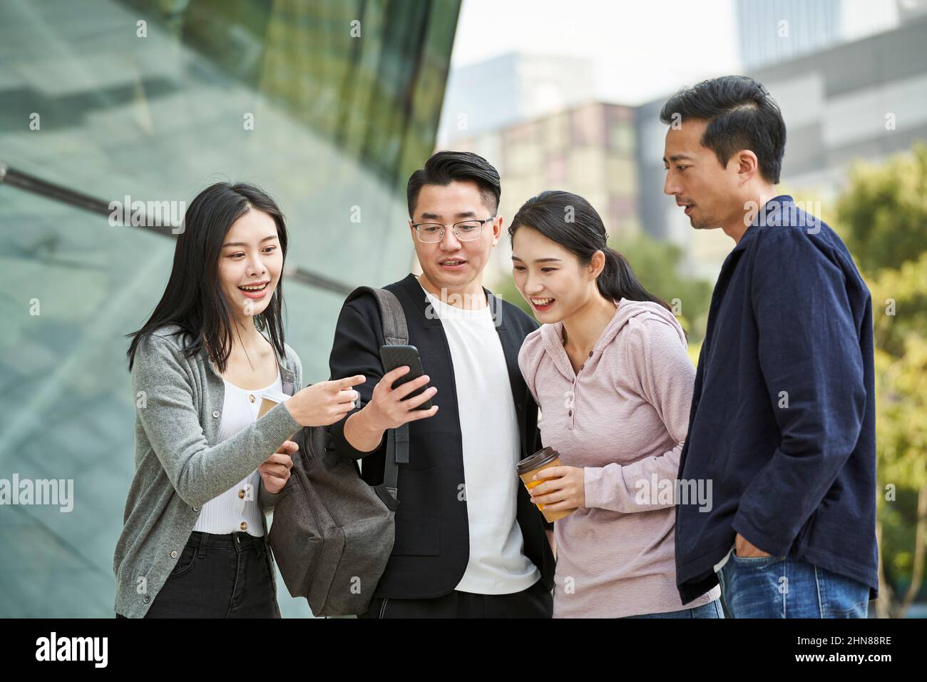 Eine Gruppe junger asiatischer Menschen, die im Freien gemeinsam das Handy angeschaut haben, glücklich und lächelnd Stockfoto