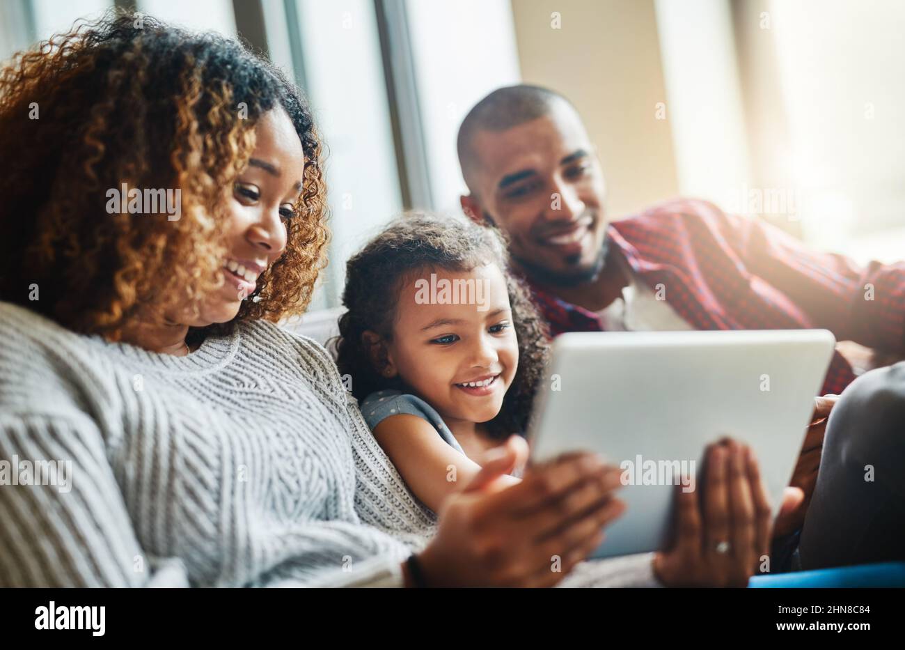 Ein technologiebewusstes kleines Mädchen aufziehen. Aufnahme eines entzückenden kleinen Mädchens und ihrer Eltern, die zu Hause ein digitales Tablet auf dem Sofa benutzen. Stockfoto