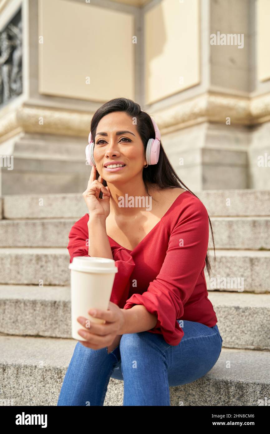 Schöne junge Frau mit Musik-Kopfhörer, hält eine Tasse Kaffee zu gehen und Musik auf einer Treppe in der Stadt zu hören. Hochwertige Fotos Stockfoto