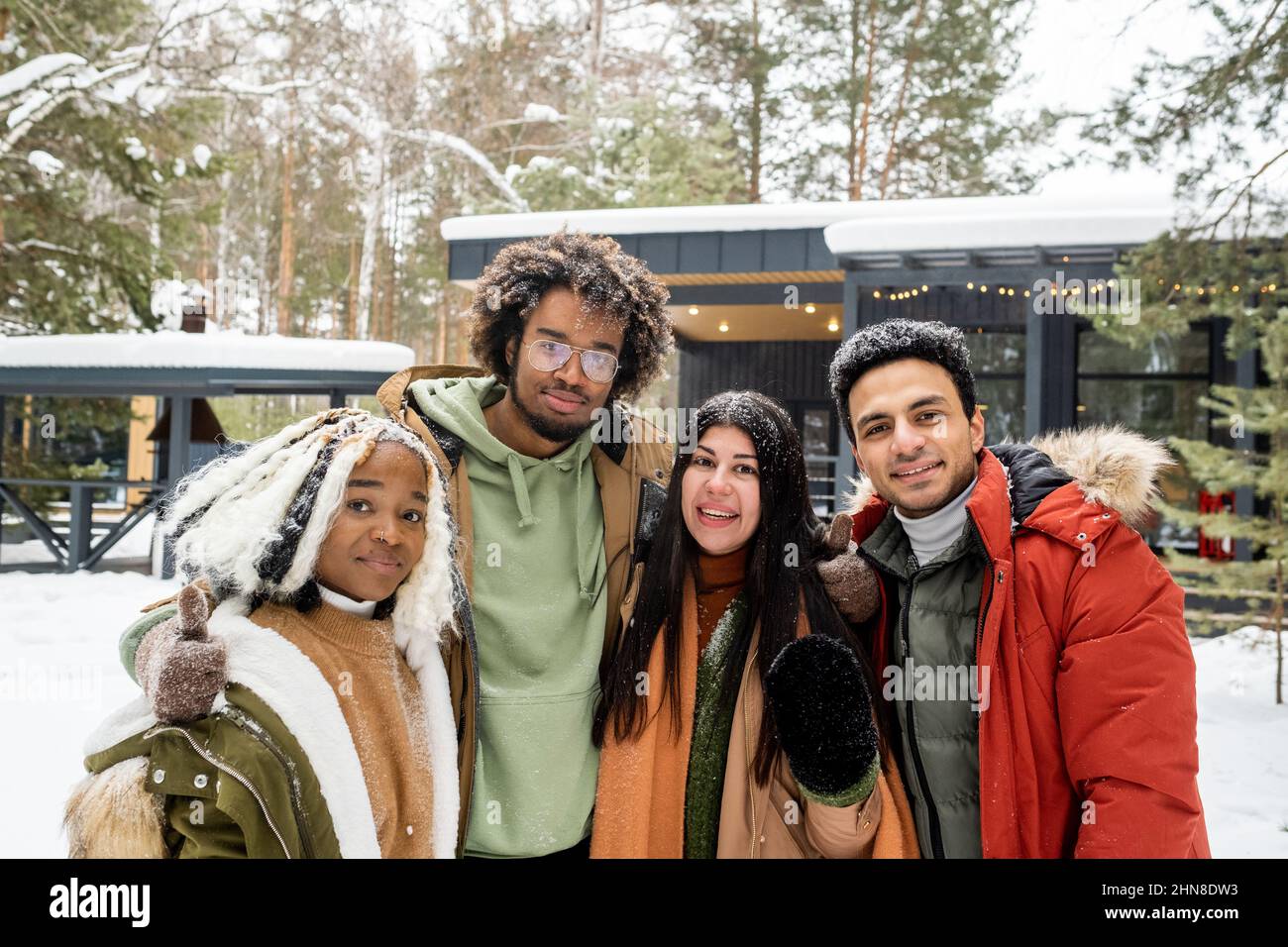 Portrait von glücklichen Freunden in warmer Kleidung, die die Kamera umarmen und lächeln, während sie im Winter im Landhaus Zeit verbringen Stockfoto