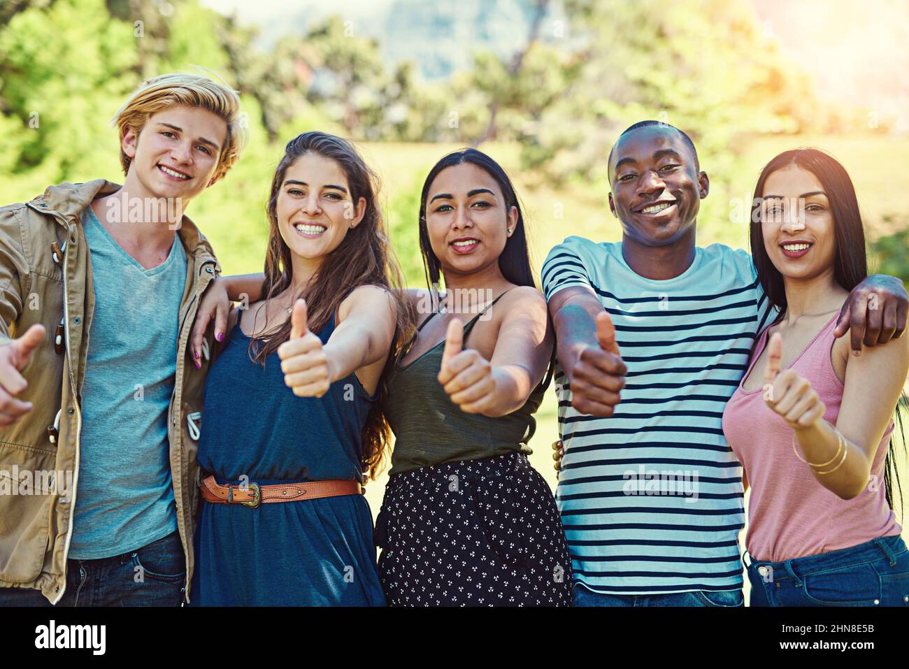 Daumen hoch für dauerhafte Freundschaften. Porträt einer Gruppe junger Freunde, die Daumen hoch zeigen, während sie zusammen im Park hängen. Stockfoto