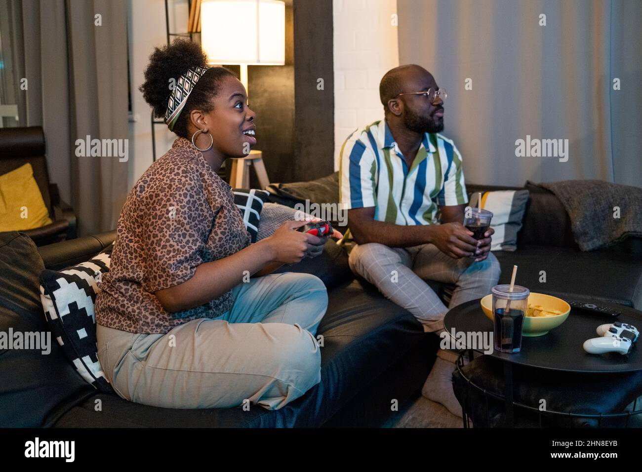 Aufgeregt Afrikanerin spielt Videospiel mit ihrem Freund für ihr Spiel zu beobachten, sie sitzen auf dem Sofa im Wohnzimmer Stockfoto