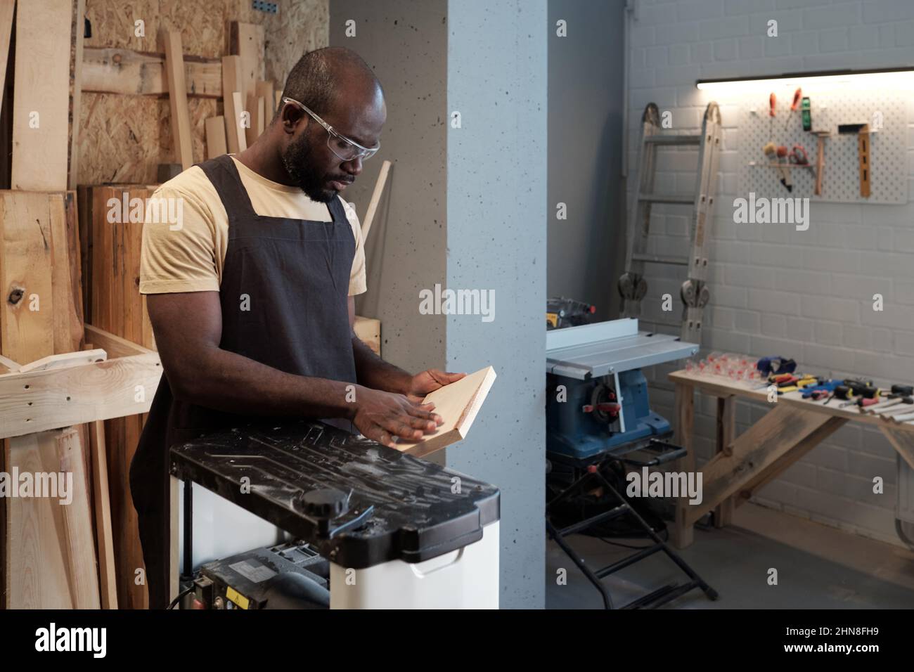 Waist-up-Porträt eines afroamerikanischen Mannes, der Holz in der Schreinerei mit Elektrowerkzeugen schneidet, Kopierraum Stockfoto