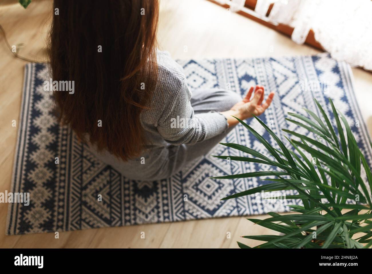 Junge Frau sitzt mit gekreuzten Beinen in der Easy Pose, in der Sukhasana-Haltung und meditiert. Yoga zu Hause üben.Glückliche junge Frau genießt sonnigen Morgen Meditationsroutine. Stockfoto