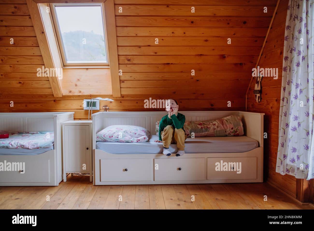 Kleiner Junge mit Down-Syndrom, der zu Hause auf dem Bett sitzt. Stockfoto