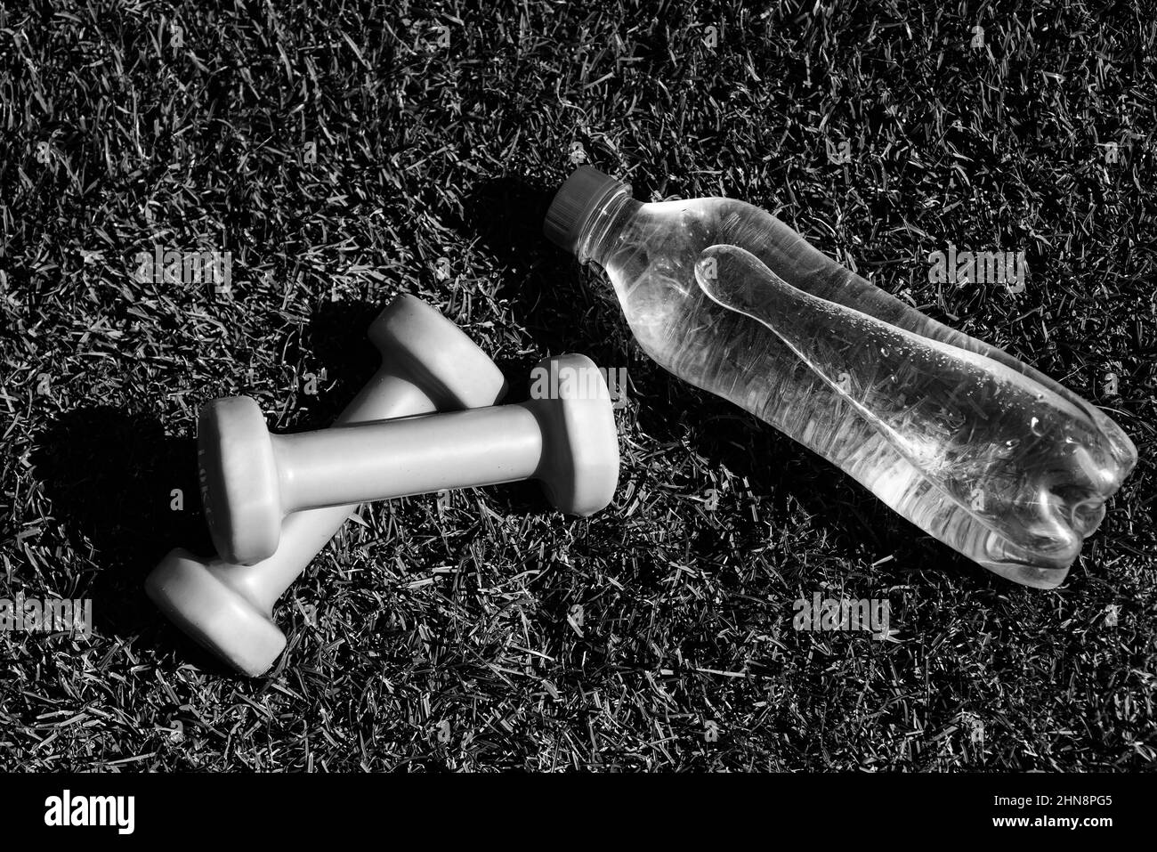 Gesunde ausgewogene Lebensweise. Pflegen Sie den Wasserhaushalt im Körper während des Trainings. Langhanteln und Flasche auf grünem Gras. Sport-Werkzeug und Ausrüstung. Hanteln in Stockfoto