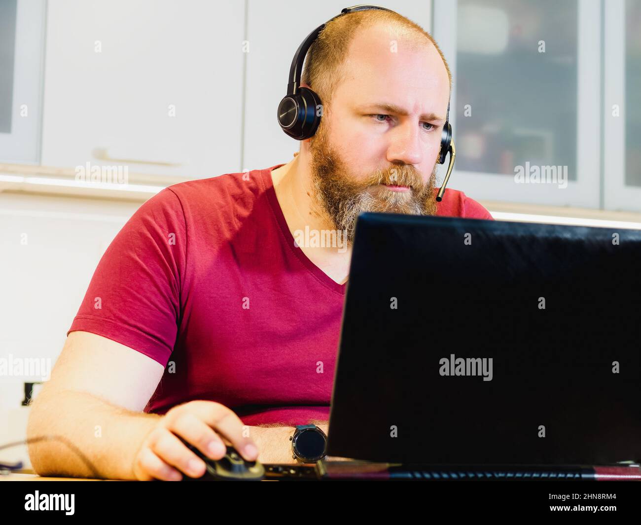 Erwachsene Person im Headset, die von zu Hause aus mit einem Laptop arbeitet. Reifer Mann konzentriert sich während Online-Meetings, Remote-Job-Konzept Stockfoto