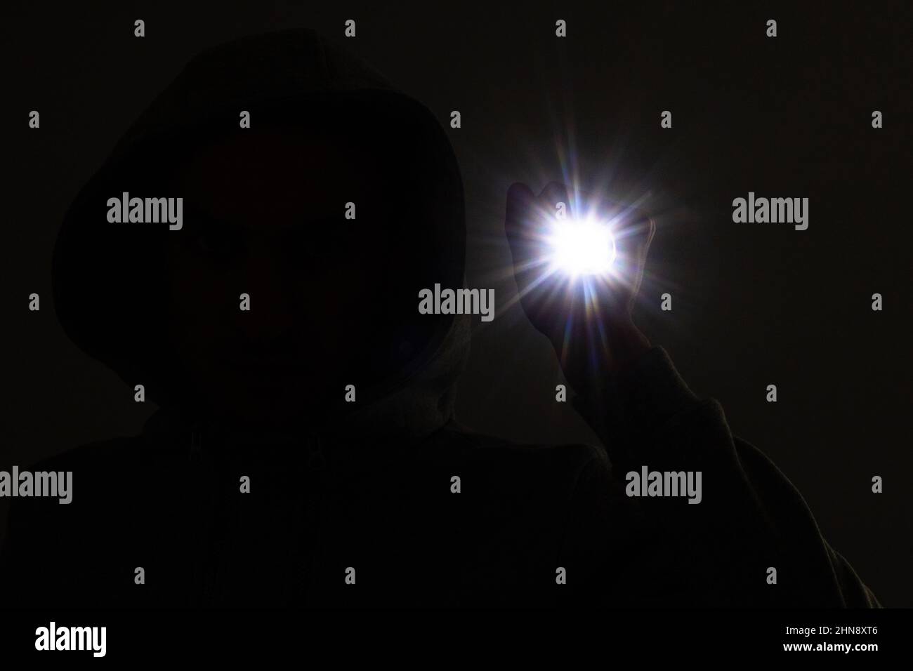 Einbrecher mit Kapuze. Silhouette von Dieb und Taschenlampe Stockfoto