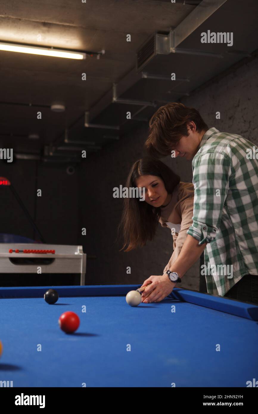 Vertikale, ausgeschnittene Aufnahme eines jungen Mannes, der seiner Freundin beim Poolspielen beibringt Stockfoto