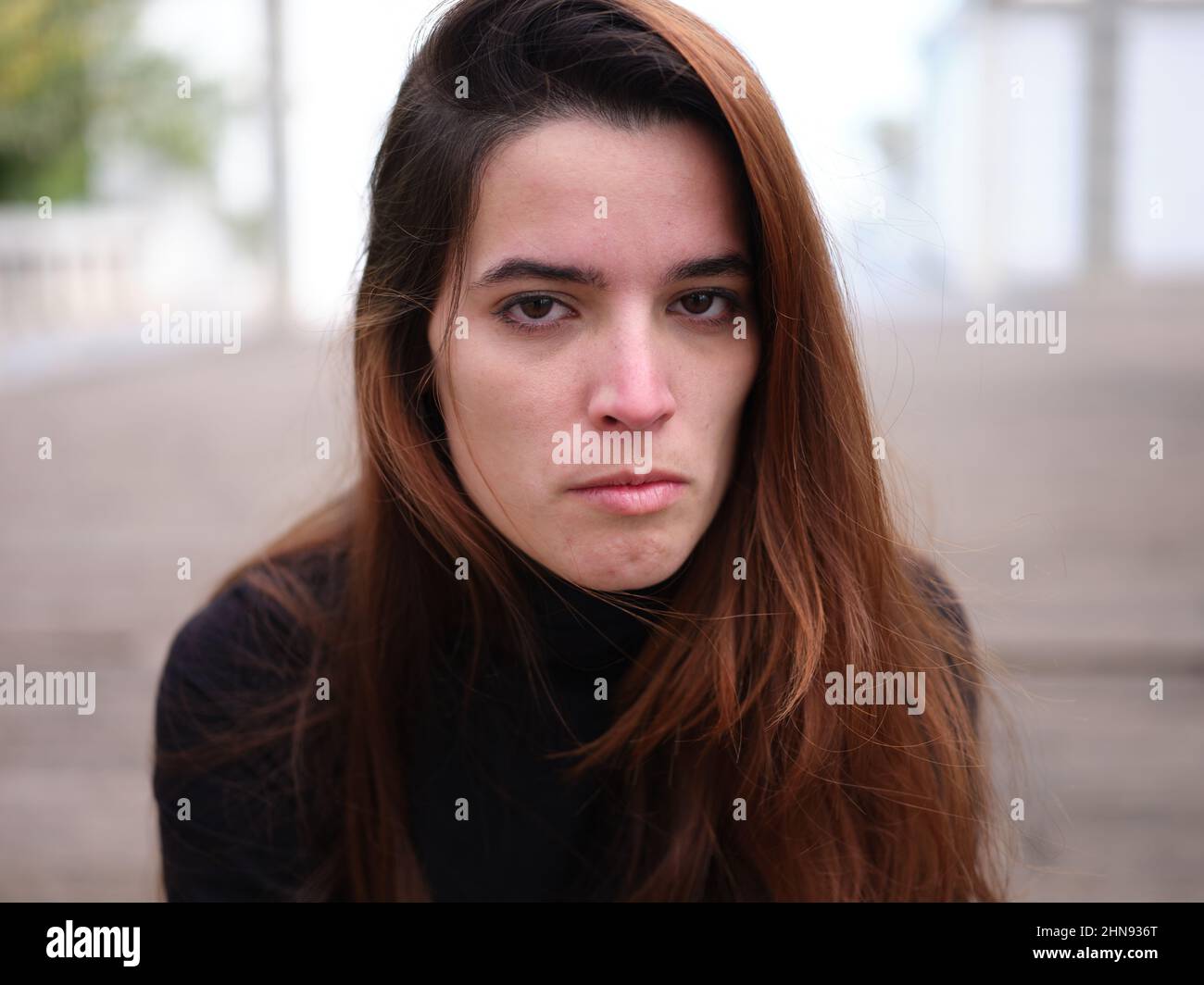 Eine zornige junge Frau, die hassvoll auf die Kamera mit einem verschwommenen Hintergrund schaut. Stockfoto