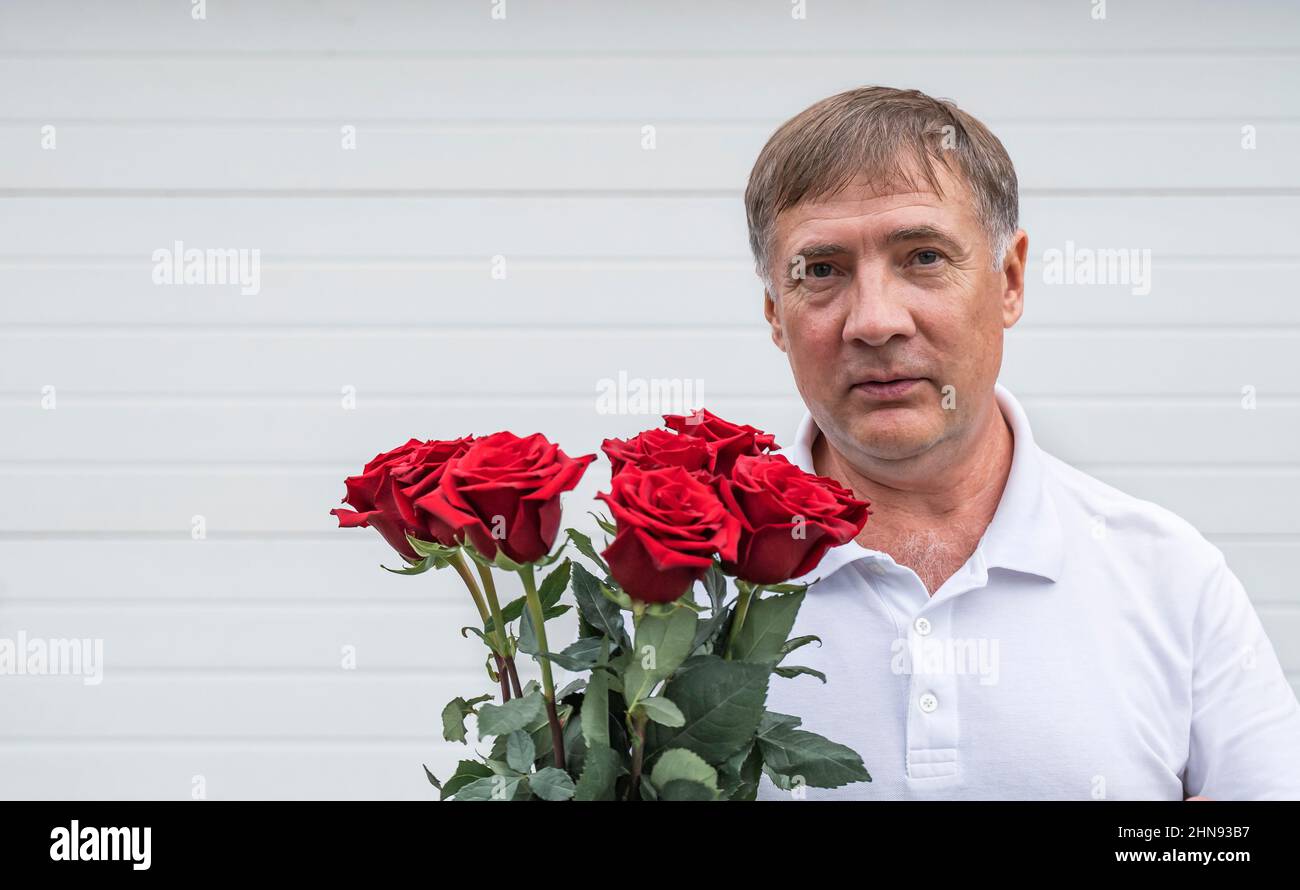 Mann mit Blumen auf hellem Hintergrund. Ein Gentleman mit einem Strauß roter Rosen schaut auf die Kamera. Stockfoto