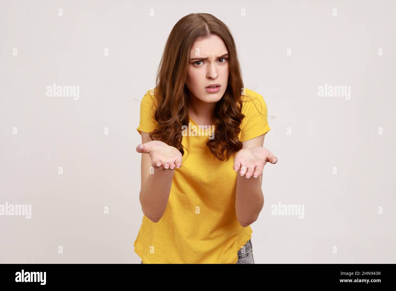 Porträt eines enttäuschten unglücklichen Teenagers in gelbem T-Shirt, das mit erhobenen Händen steht und fragt, was du willst, wütendes Gesicht. Innenaufnahme des Studios isoliert auf grauem Hintergrund. Stockfoto