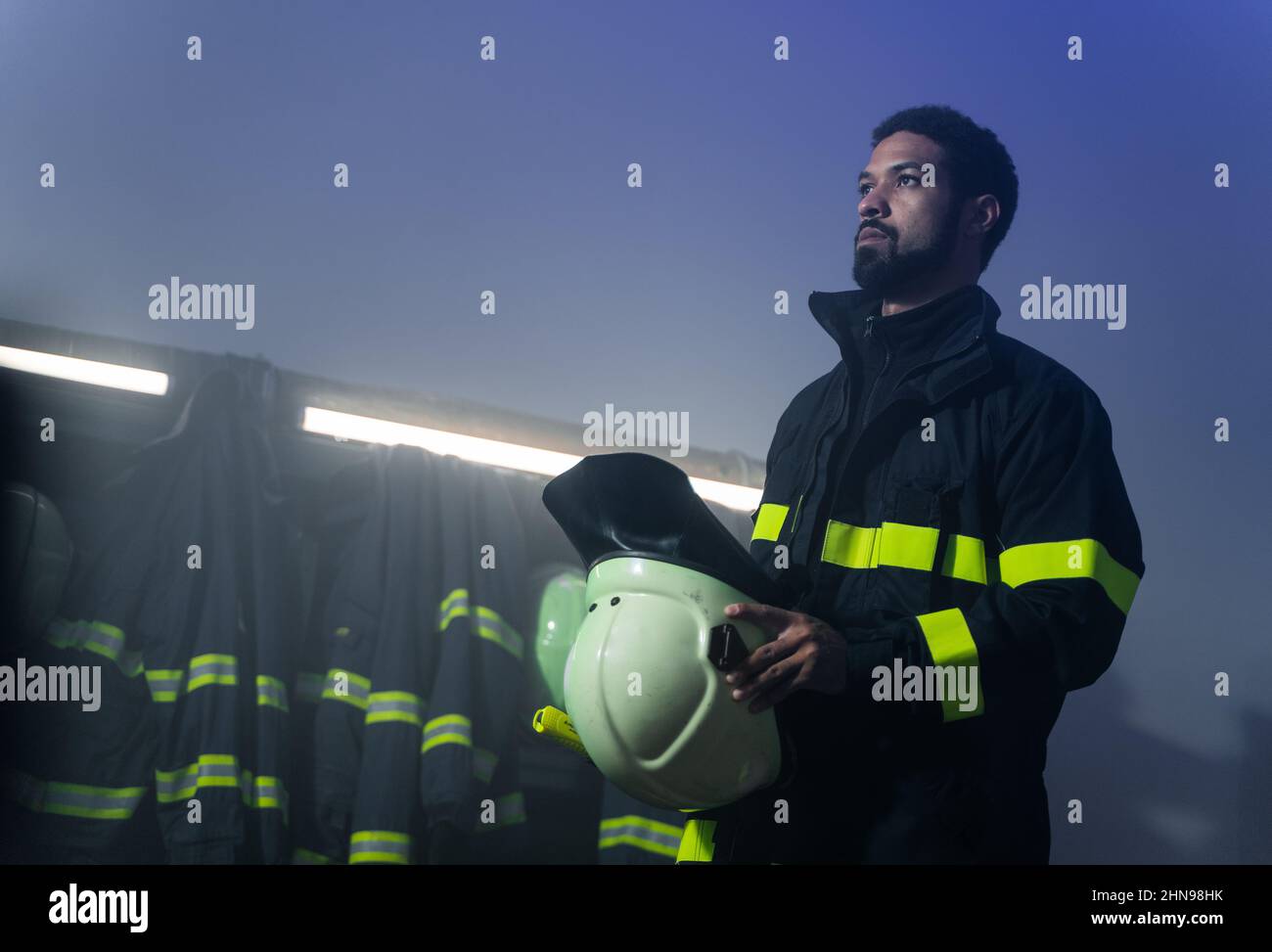 Low-Angle-Ansicht des jungen afroamerikanischen Feuerwehrmann Vorbereitung auf den Einsatz in der Feuerwehr in der Nacht. Stockfoto