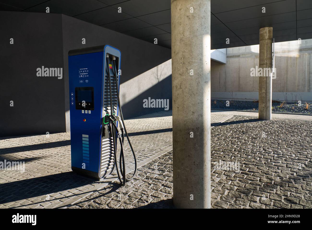 Blue Electric Vehicle Charging Station neben einem Betonmast auf dem Parkplatz Stockfoto