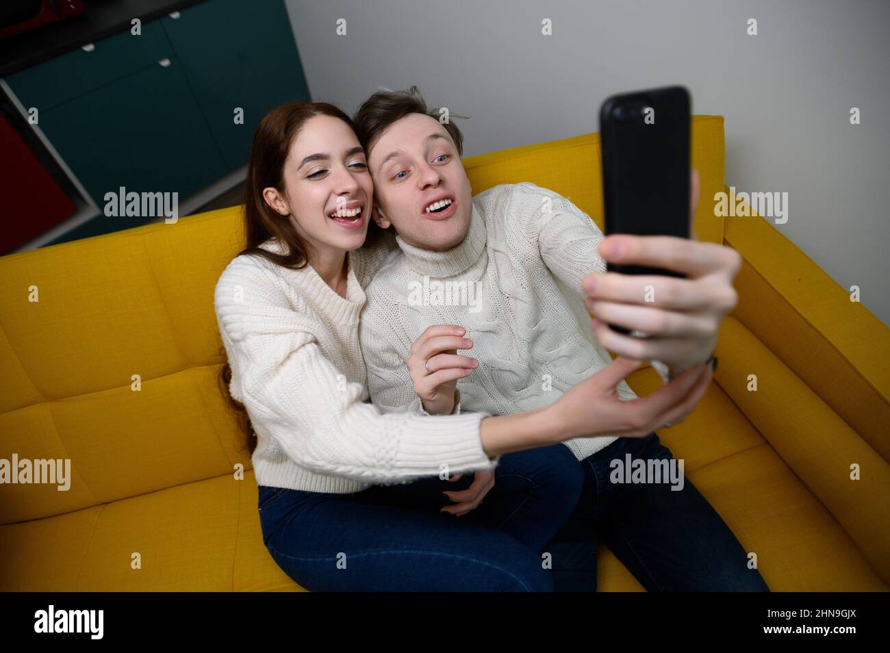 Positives junges Paar, das zu Hause auf dem Sofa sitzt und Selfie nimmt Stockfoto