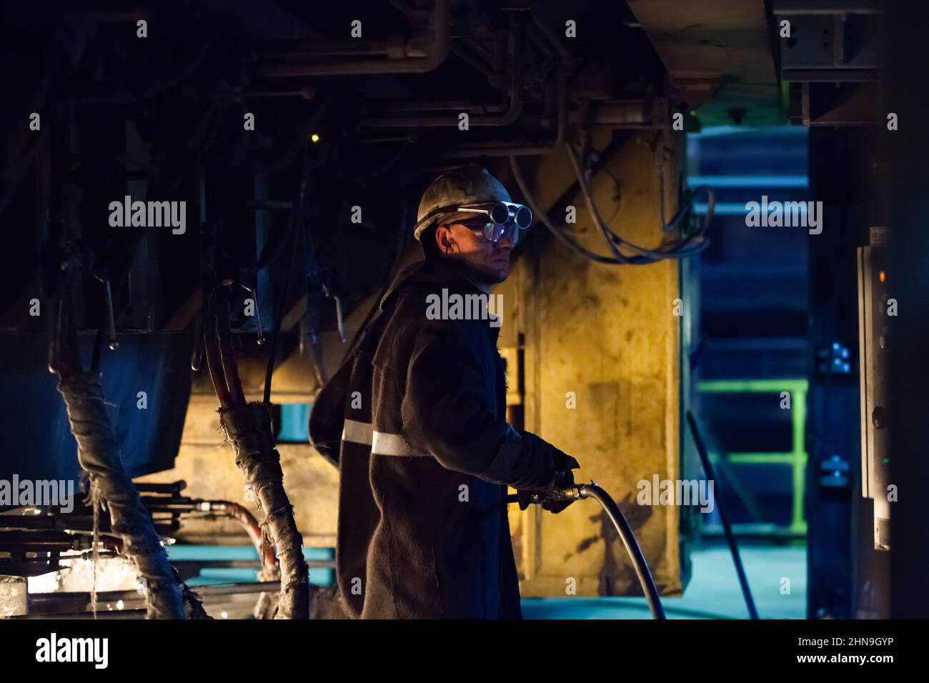 Temirtau, Kasachstan - 08. Juni 2012: Metallurgie-Anlage von Arcelor Mittal. Metallurge in Filz-Wärmeschutzanzug und Brille. Gummischlauch mit Ochse festhalten Stockfoto