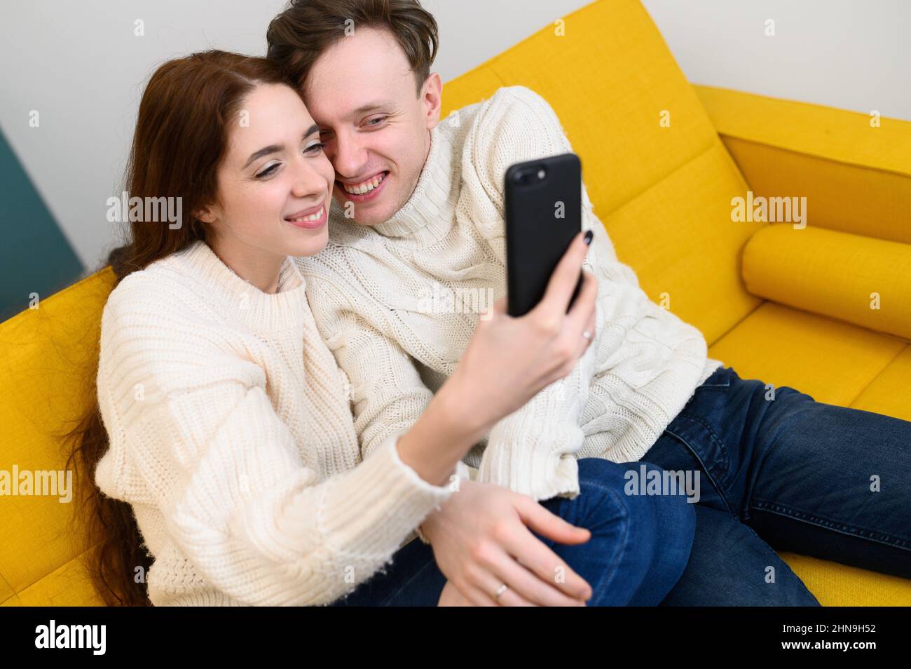 Positives junges Paar, das zu Hause auf dem Sofa sitzt und Selfie nimmt Stockfoto
