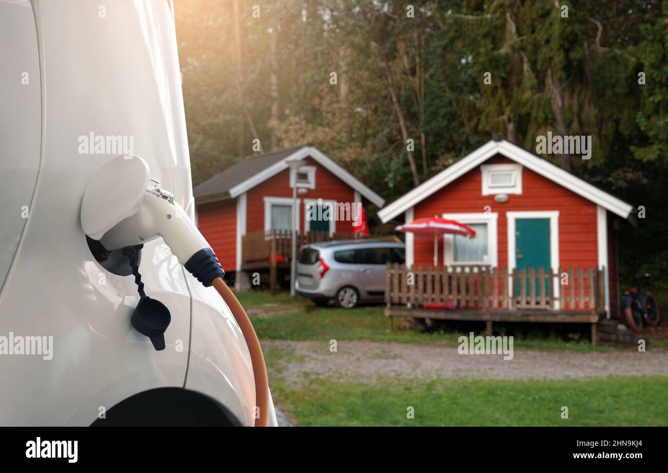 Nahaufnahme eines Ladekabels, das mit einem Elektroauto vor der Kulisse eines Campingplatzes verbunden ist Stockfoto