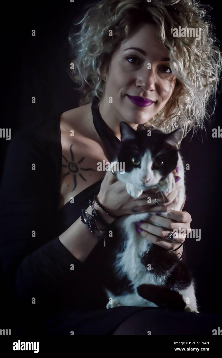 Porträt einer schönen lockigen und lächelnden blonden Frau mit einer schwarz-weißen Katze Stockfoto