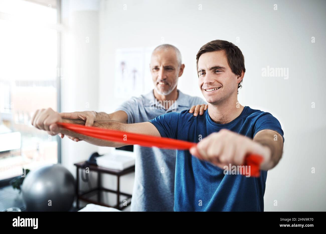 Halten Sie Ihre Bewegungen ruhig und langsam. Aufnahme eines Physiotherapeuten, der einem Patienten hilft, sich mit Widerstandsbändern zu dehnen. Stockfoto