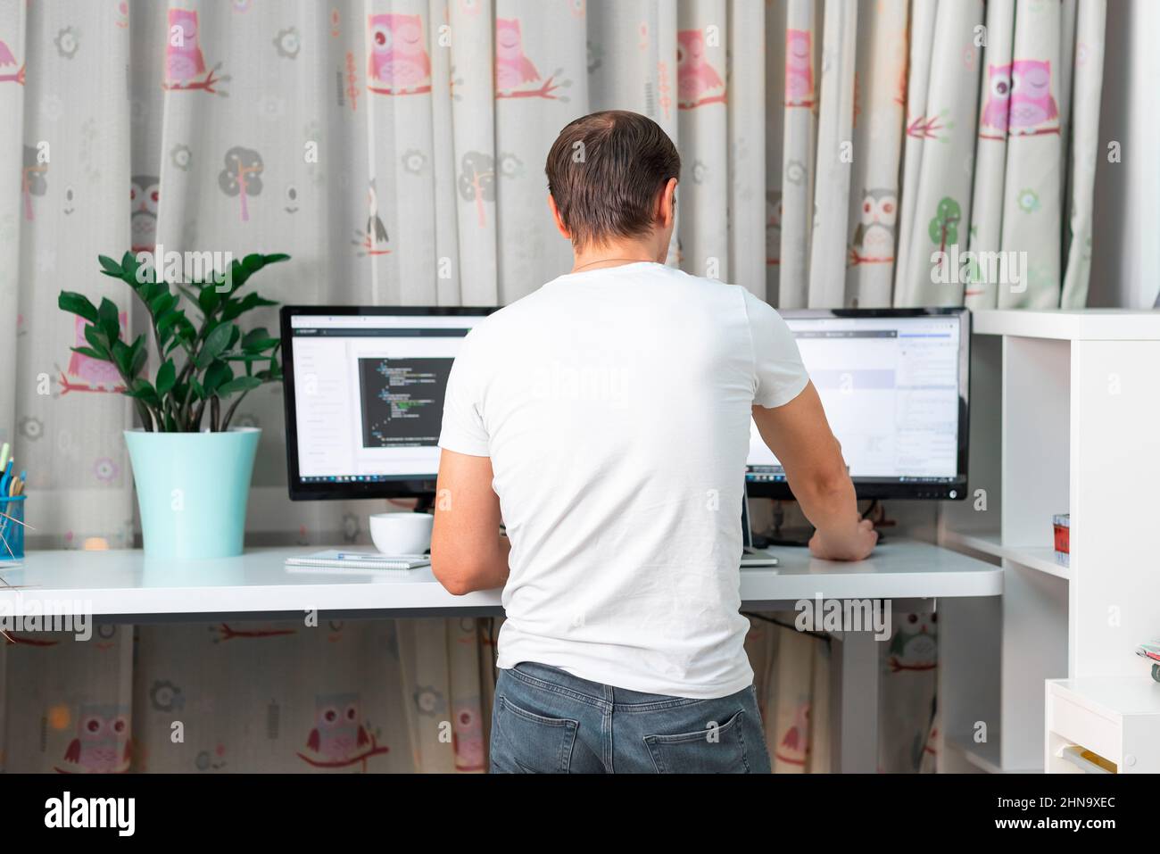 Mann, der im Heimbüro auf dem Schreibtisch am Computer arbeitet. Freiberuflicher Mitarbeiter, der von zu Hause aus arbeitet. Hoher Stehtisch bequem für gesunden Rücken Stockfoto