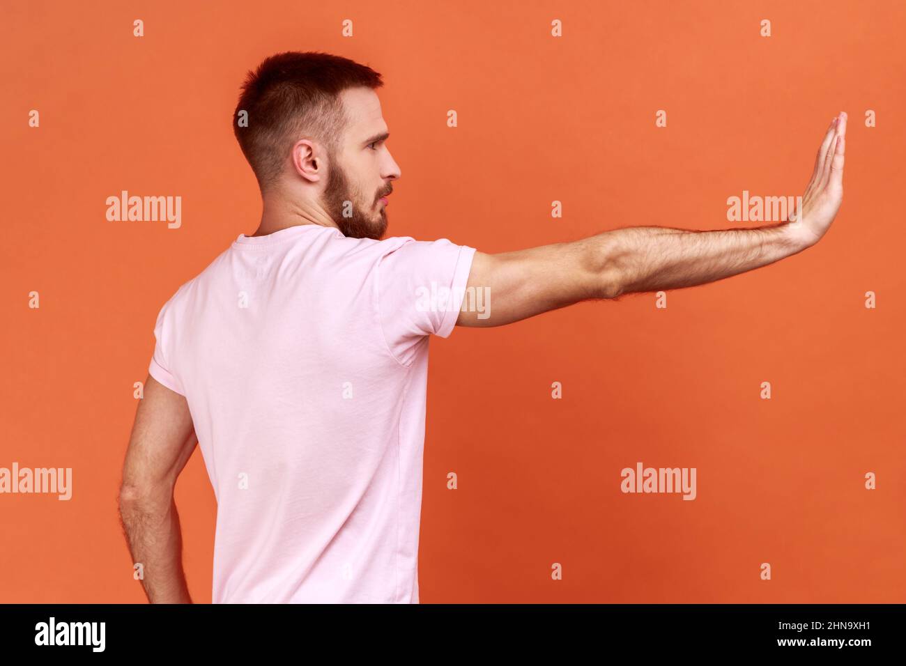 Seitenansicht eines ernsthaften Mannes, der eine Stop-Geste mit Handfläche macht, Warnung vor Gefahren durch Konfliktverbote, Mobbing stoppen, pinkes T-Shirt tragen. Innenaufnahme des Studios isoliert auf orangefarbenem Hintergrund. Stockfoto