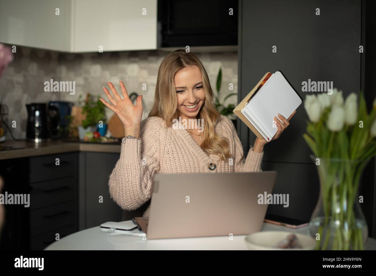 Junge lächelnde schöne Frau mit langen welligen hellen Haaren in beigefarbenem Pullover Begrüßung Gespräch auf Webcam virtuelle Konversation. Stockfoto