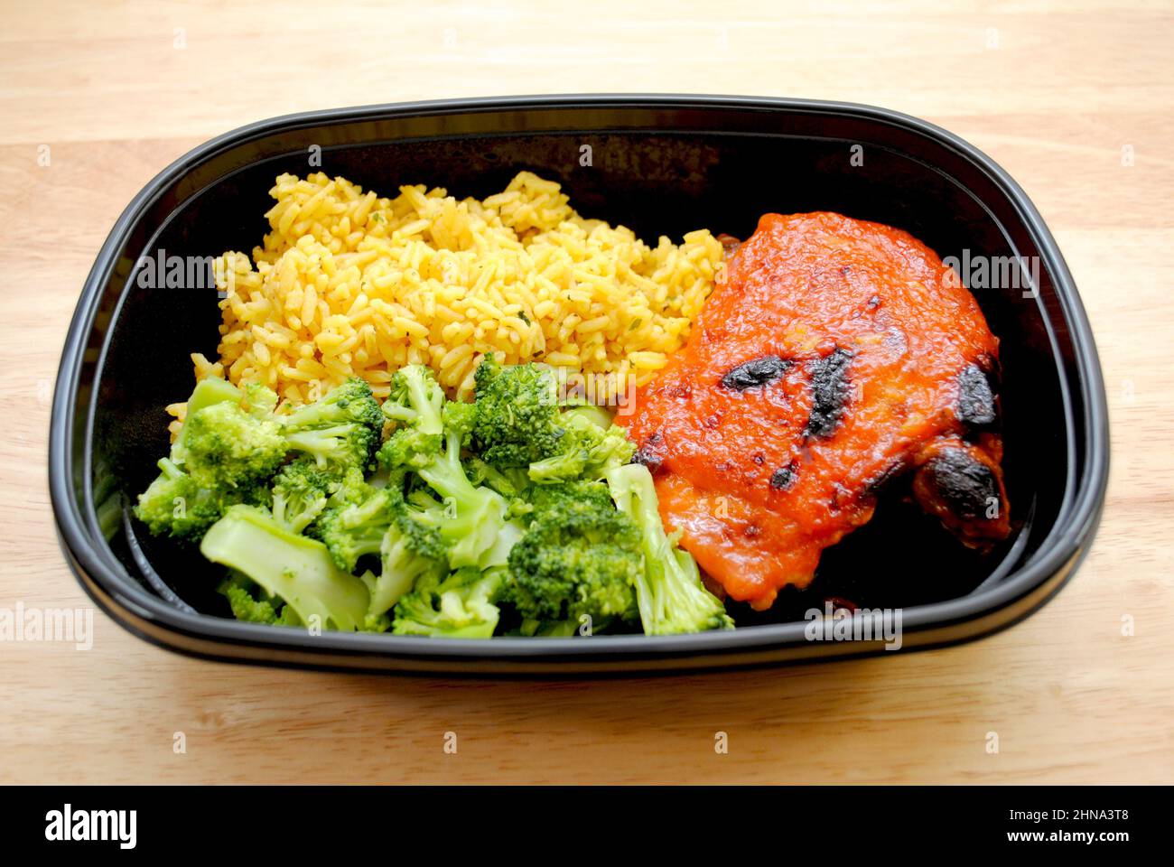 Eine Mahlzeit mit einem Chicken Thigh mit Catalina Dressing Oben gebacken, gelbem Reis und gedünstetem Broccoli Stockfoto