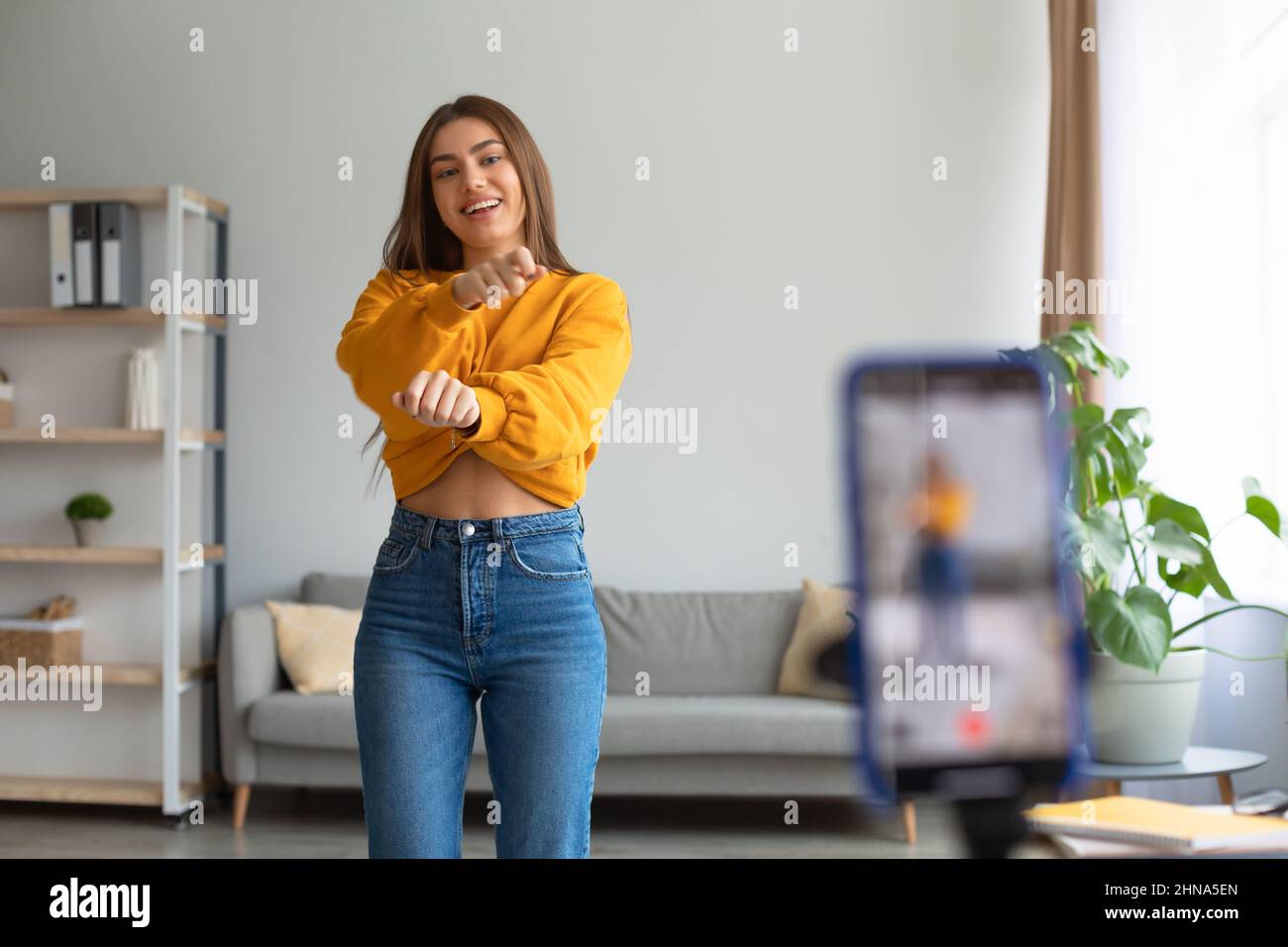 Junge kaukasische Influencerin, die Videos auf dem Smartphone aufzeichnet und zu Hause vor der Kamera tanzt Stockfoto