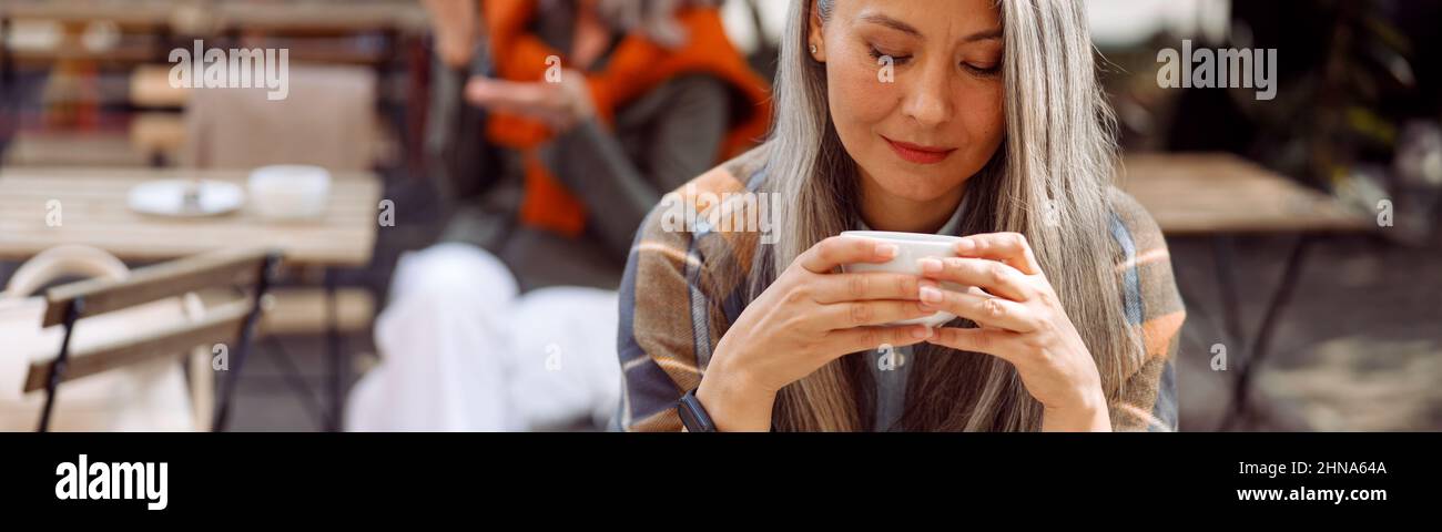 Ältere Cafe-Gäste, konzentrieren sich auf eine hübsche silberhaarige Dame, die eine Tasse Getränk hält Stockfoto