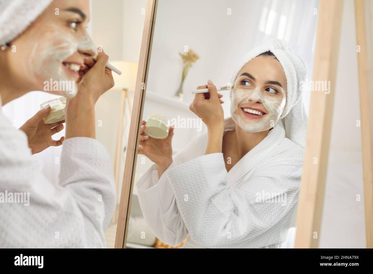 Reflexion im Spiegel der schönen jungen Frau mit Pinsel gilt kosmetische Maske für Gesicht. Stockfoto