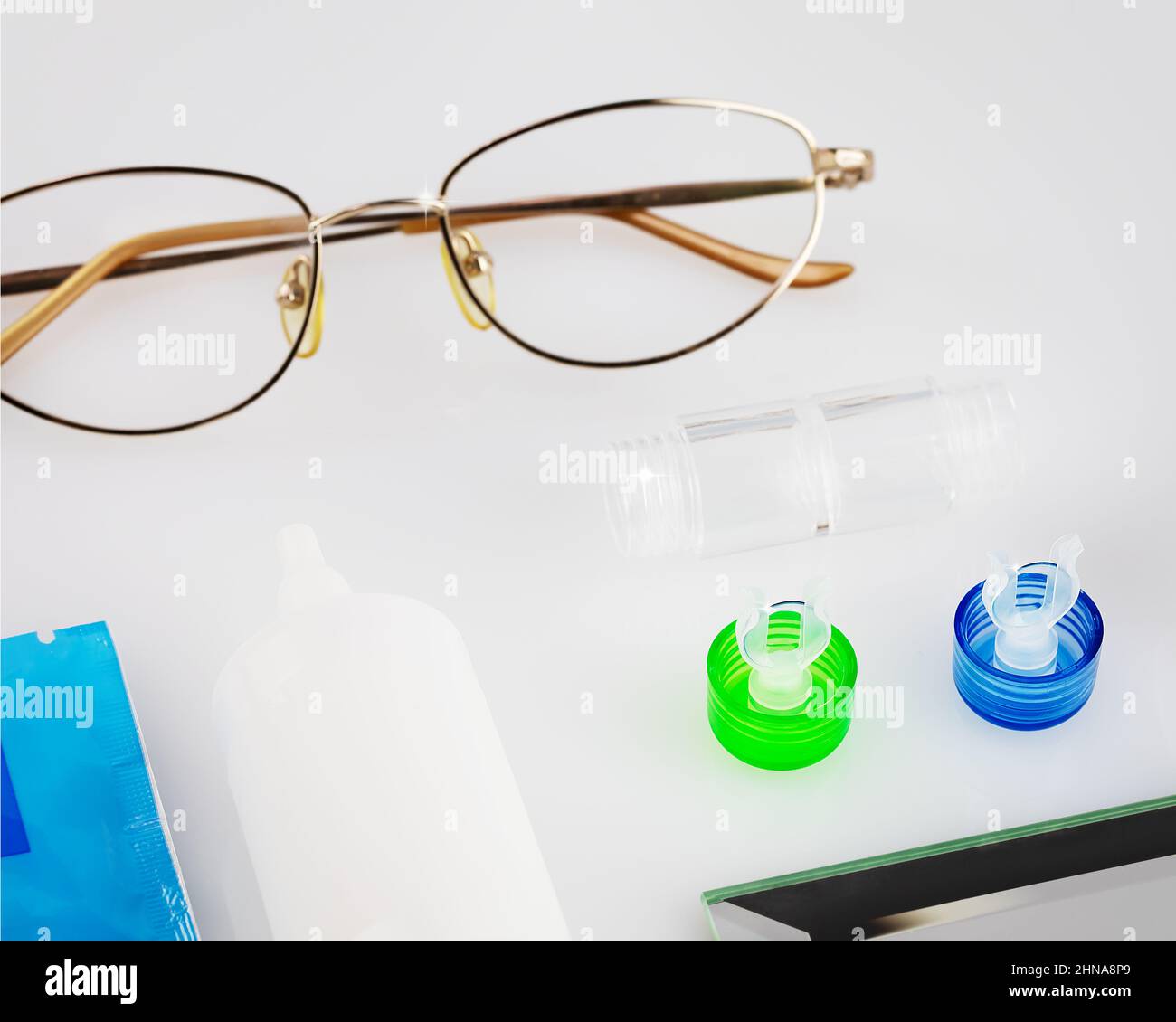 Kontaktlinsen-Set mit Linsen, Behälter, Brille und Augentropfen auf einem weißen Tisch. Das Konzept der richtigen Verwendung von Kontakt- und Nachtlinsen und deren Pflege. Stockfoto