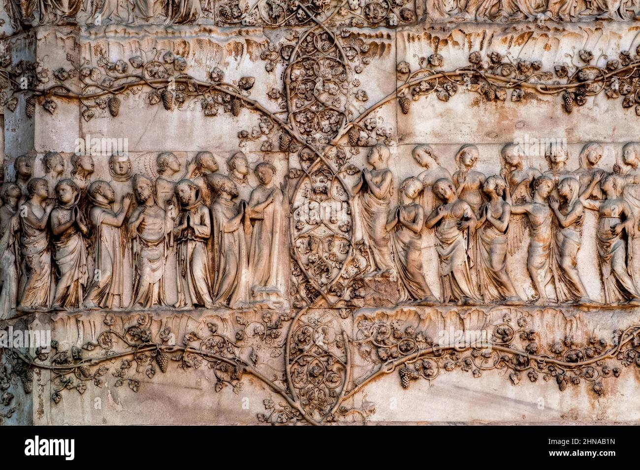 Heilige und Engel eingerahmt von blühenden Weinreben aus dem 1300 letzten Jüngsten Jüngsten Jüngsten Jüngsten Jüngsten Jüngsten Marmor an der Westfront der Kathedrale von Orvieto, Umbrien, Italien. Diese Skulptur wird Lorenzo Maitani (ca. 1275–1330) zugeschrieben, der die spätgotische Fassade der Kathedrale entwarf. Maitani soll als Bildhauer direkt auf zwei Tafeln eingegangen sein, die zwei der vier unteren Pilaster der Fassade bedecken: Eine Maitani-Platte zeigt Szenen aus dem Jüngsten Gericht, einschließlich der Szene in diesem Bild. Stockfoto