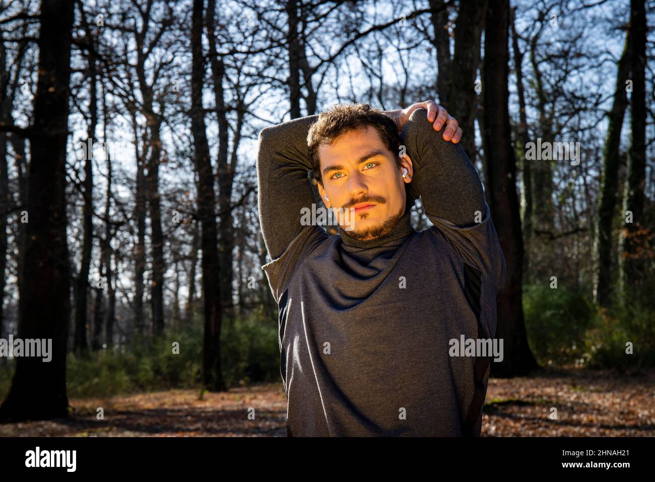 Läufer streckt sich beim Musikhören. Der junge Mann bildet im Wald aus. Konzept von Sport und Wellness. Stockfoto