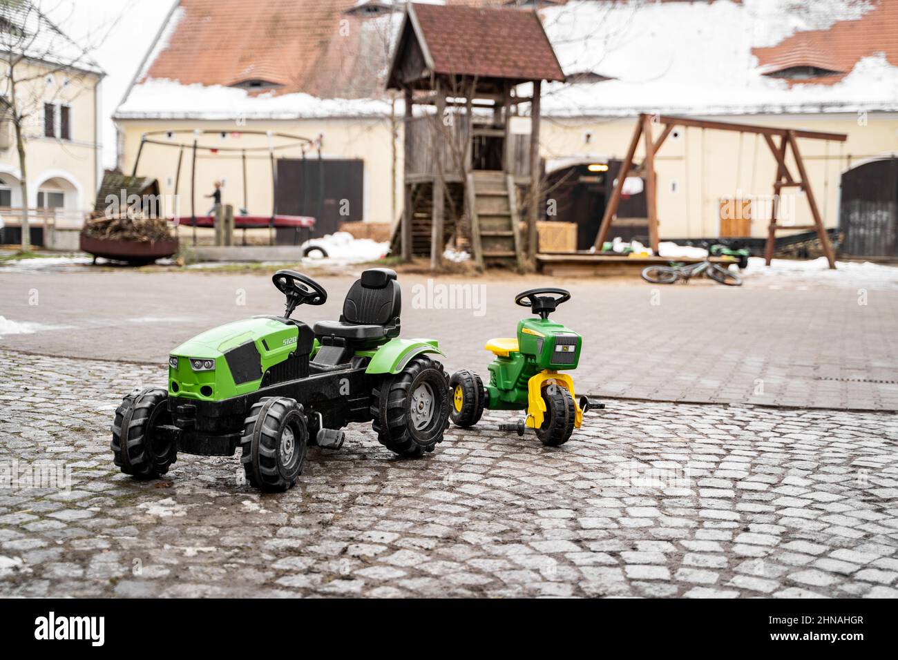 Grüne künstliche Traktor Kinder Spielzeug auf Bauernhof oder Hinterhof am Tag im Winter Stockfoto